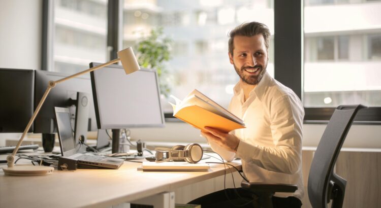 Arbeitszufriedenheit: Mann sitzt an einem Büroarbeitsplatz und lächelt