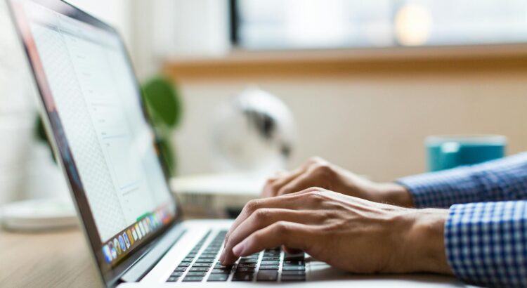 Die Hände eines Menschen tippen auf der Tastatur eines geöffneten Laptops
